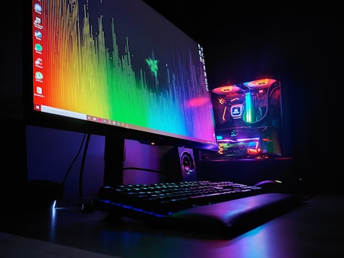 Monitor con gradiente arcoiris junto a torre de PC con luces RGB